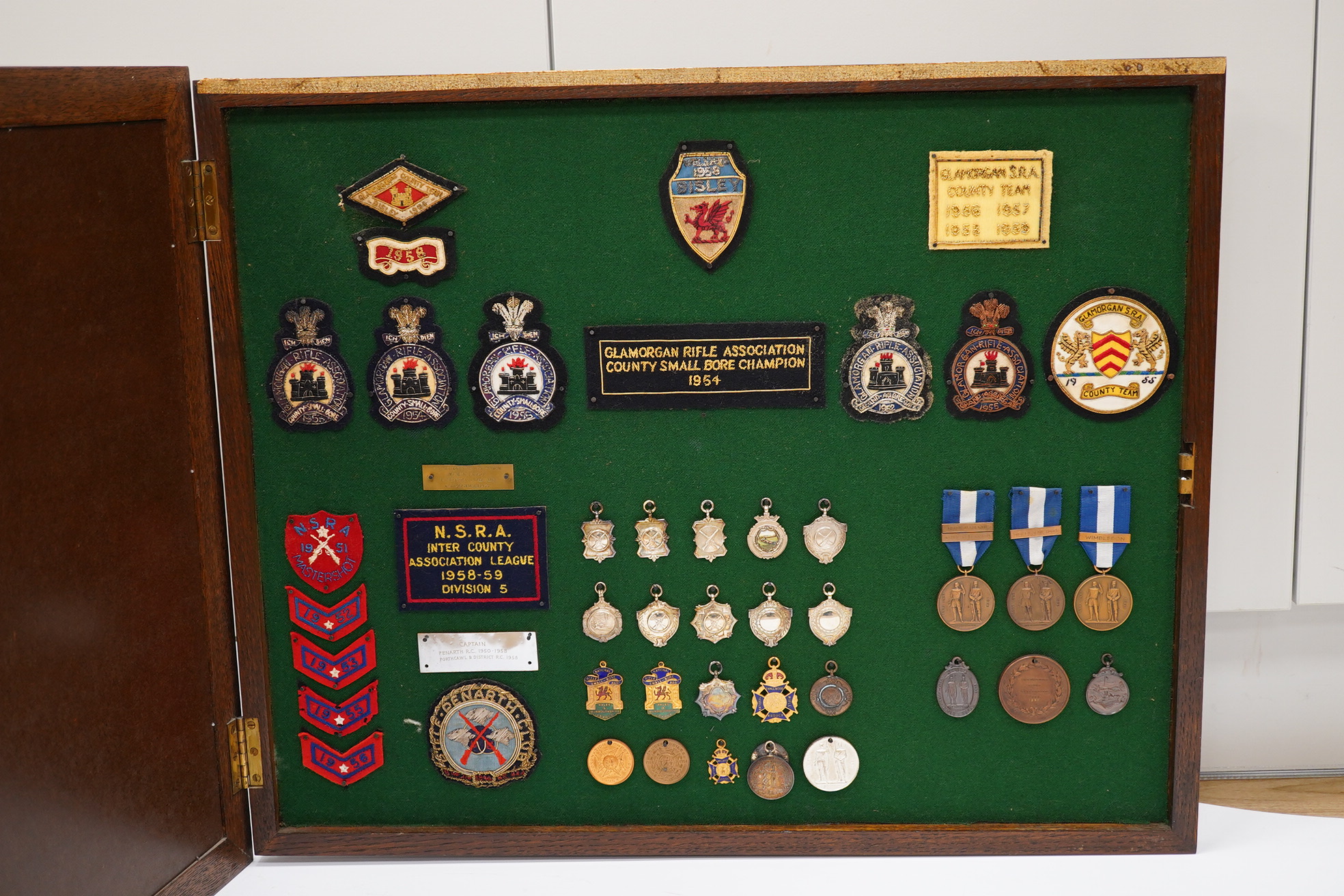 An oak cased collection of rifle and shooting medals disguised as a framed map of Glamorganshire, containing hallmarked silver medals engraved to the awardees, cloth badges for Glamorgan Rifle Association, bronze rifle a